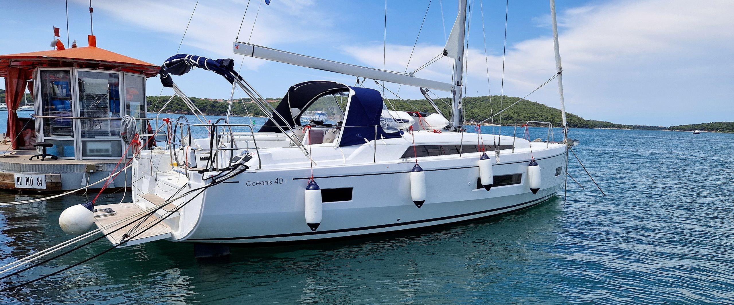 A white yacht docked at a marina with a clear view of the water and a distant shoreline.