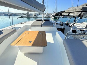 A boat deck with a cushioned seating area, a wooden table, and a view of other boats at a marina. - Sun-Kissed Sailing Adventure in Zadar, Croatia (Bibinje)