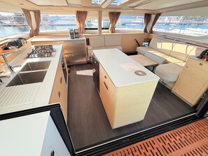 Eine kleine Kombühe mit Spüle, Herd und Stauräumen, eine gemütliche Sitzecke und Blick auf den Hafen.