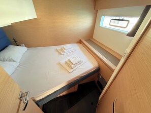 Ein kleines Zimmer mit Bett, zwei Handtüchern, einem Fenster und einem kleinen Tisch.