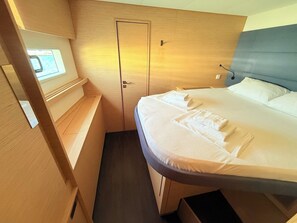 Quarto compacto com uma cama, uma janela pequena, uma porta e um banco embutido.
