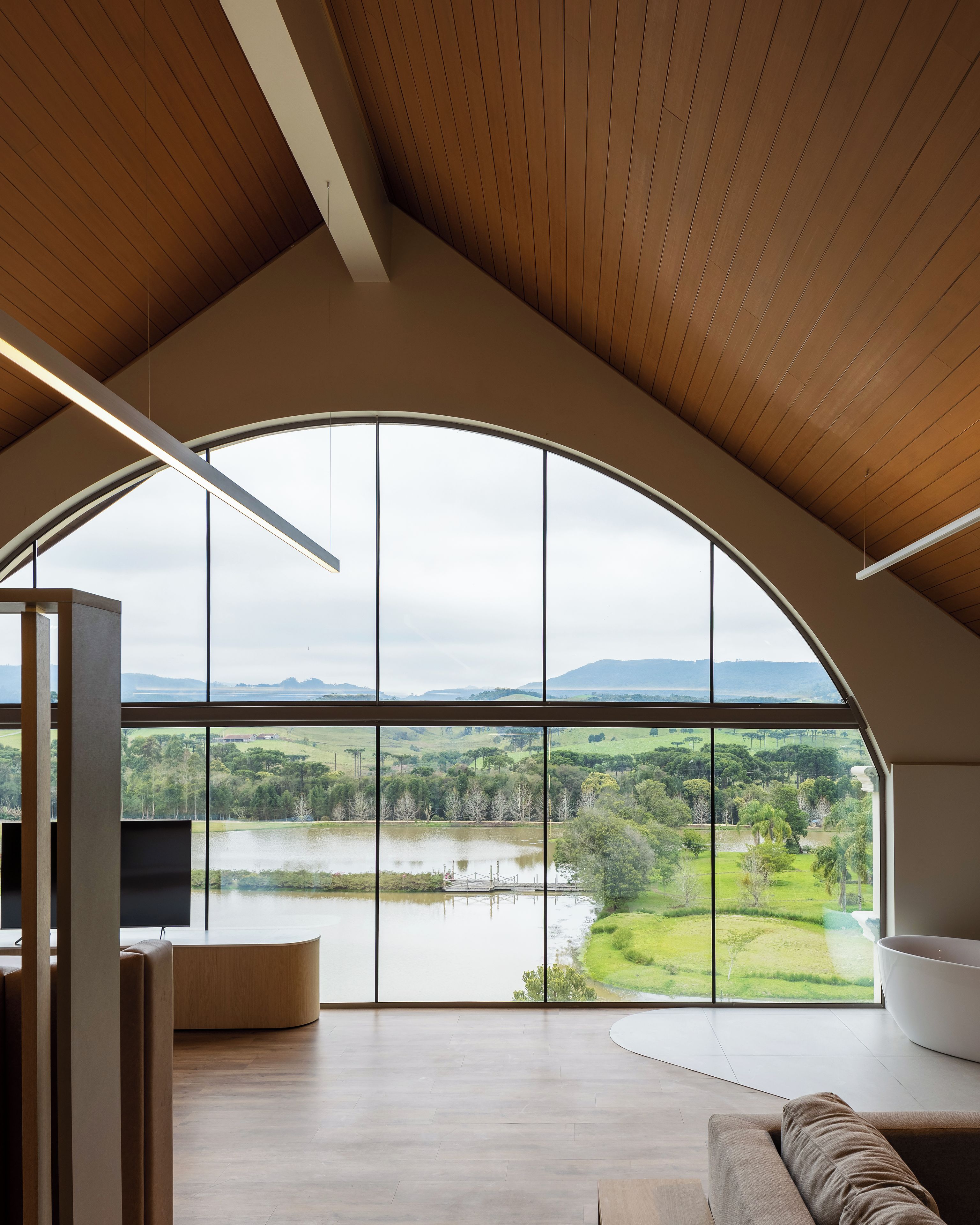 A spacious room with a large arched window offering a view of a lake and surrounding landscape.