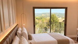 Une chambre avec une grande fenêtre, un lit recouvert de plusieurs coussins et un luminaire suspendu.
