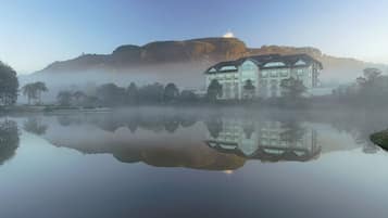 A large building with multiple floors and a flat roof, situated near a calm body of water with a reflection.