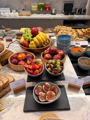 A buffet with various fruits, pastries, and a coffee machine.