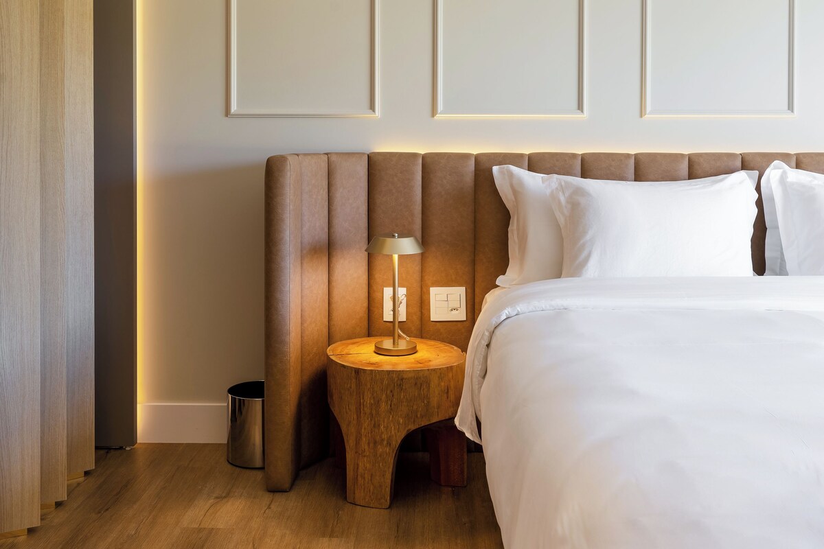 Hotellihuone, jossa on suuri sänky, yöpöytä lampun kanssa, puulattia ja seinäpaneeli.