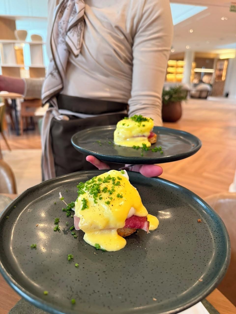 A person holding a plate with a dish that appears to be a type of egg-based entrée, possibly a poached egg or an egg sandwich, garnished with green herbs.