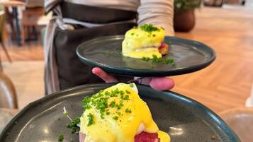 A person holding a plate with a dish that appears to be a type of egg-based entrée, possibly a poached egg or an egg sandwich, garnished with green herbs.