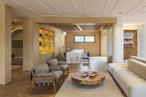 A modern interior with a wooden floor, a round wooden coffee table, a sofa, and a dining area with a marble table and chairs. - Montissi Resort Spa (Rancho Queimado)