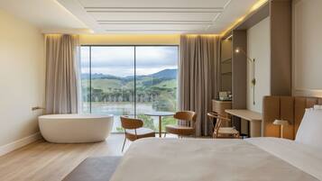 Une chambre d’hôtel moderne dotée d’un grand lit, d’une baignoire, d’une table à manger et offrant une vue sur un lac et des montagnes.