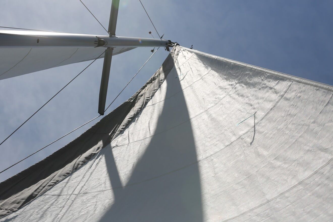 Der Mast und die Segel eines Segelbootes vor blauem Himmel.
