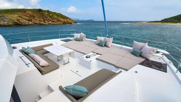 Le pont d’un yacht, avec des sièges, une table et une vue sur la mer et la côte.
