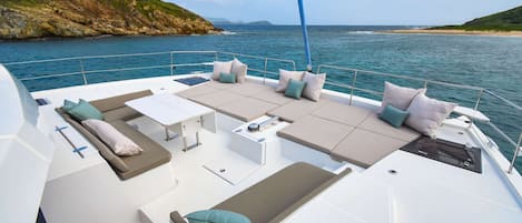 A yacht's deck with seating, a table, and a view of the sea and coastline.