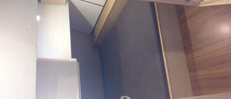 A narrow, enclosed bathroom with a wooden vanity, a white sink, and a dark-colored shower area.