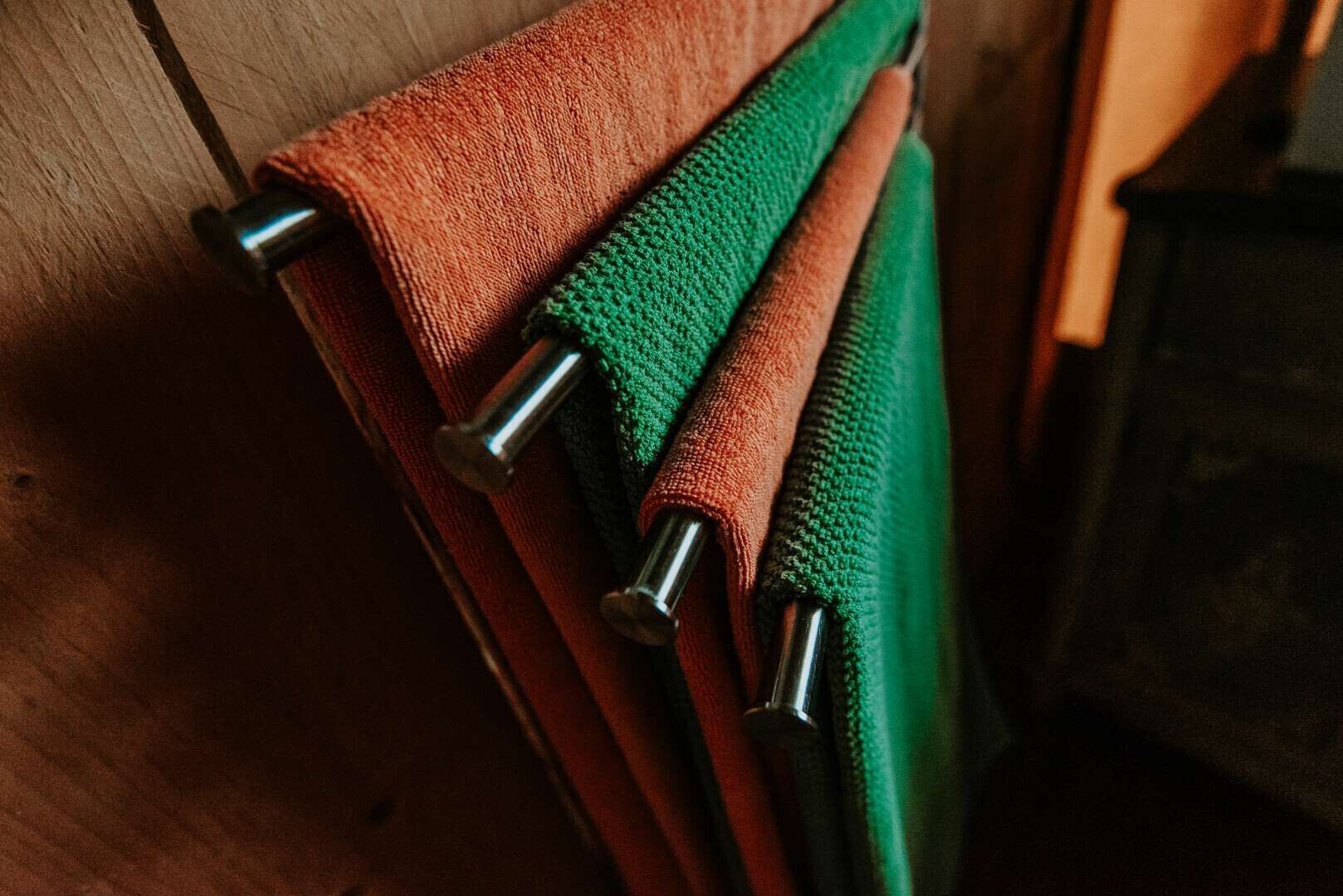 A wooden surface with three towels rolled up and secured with metal clips.