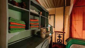 Une pièce comprenant un lit, une étagère avec des serviettes pliées, une chaise en bois et une table sur laquelle se trouvent une carafe et un bol.