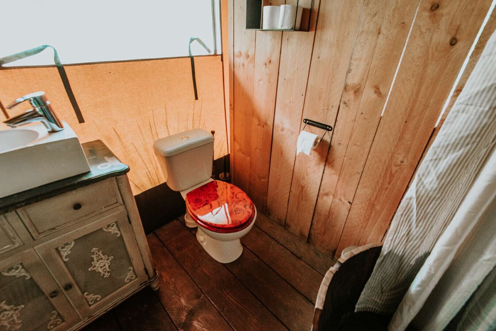 Pieni, käytännöllinen kylpyhuone, jossa on puulattia, valkoinen wc-istuin, puinen allaskaappi peilillä sekä pyyhe, joka on ripustettu seinälle.