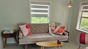 Een woonkamer met een bank, een klein houten tafeltje, een rode stoel en een vloerlamp.