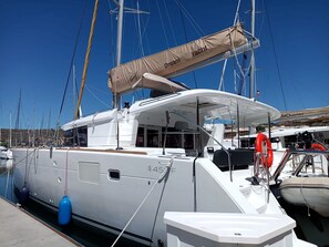 A marina with a white yacht docked, featuring a cabin with a large window, a lifebuoy, and a sail cover labeled 'Dream Yacht.'