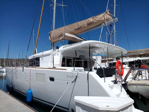 A marina with a white yacht docked, featuring a cabin with a large window, a lifebuoy, and a sail cover labeled 'Dream Yacht.'