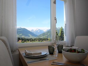 A dining table with a view of mountains, a bowl of salad, and a wine glass. - Kitty (Parterre) Appartement/Fewo, Dusche oder Bad, WC 4-Bettwohnung by Interhome (Gstaad)