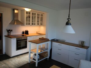 Uma cozinha compacta com armários brancos, forno embutido, bancada de madeira e luminária pendente.