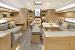 A modern interior with a central dining area, two sofas, a bench, and a staircase leading to an upper level. - Sun-Kissed Sailing Adventure in Islas Baleares, Mallorca (Palma)