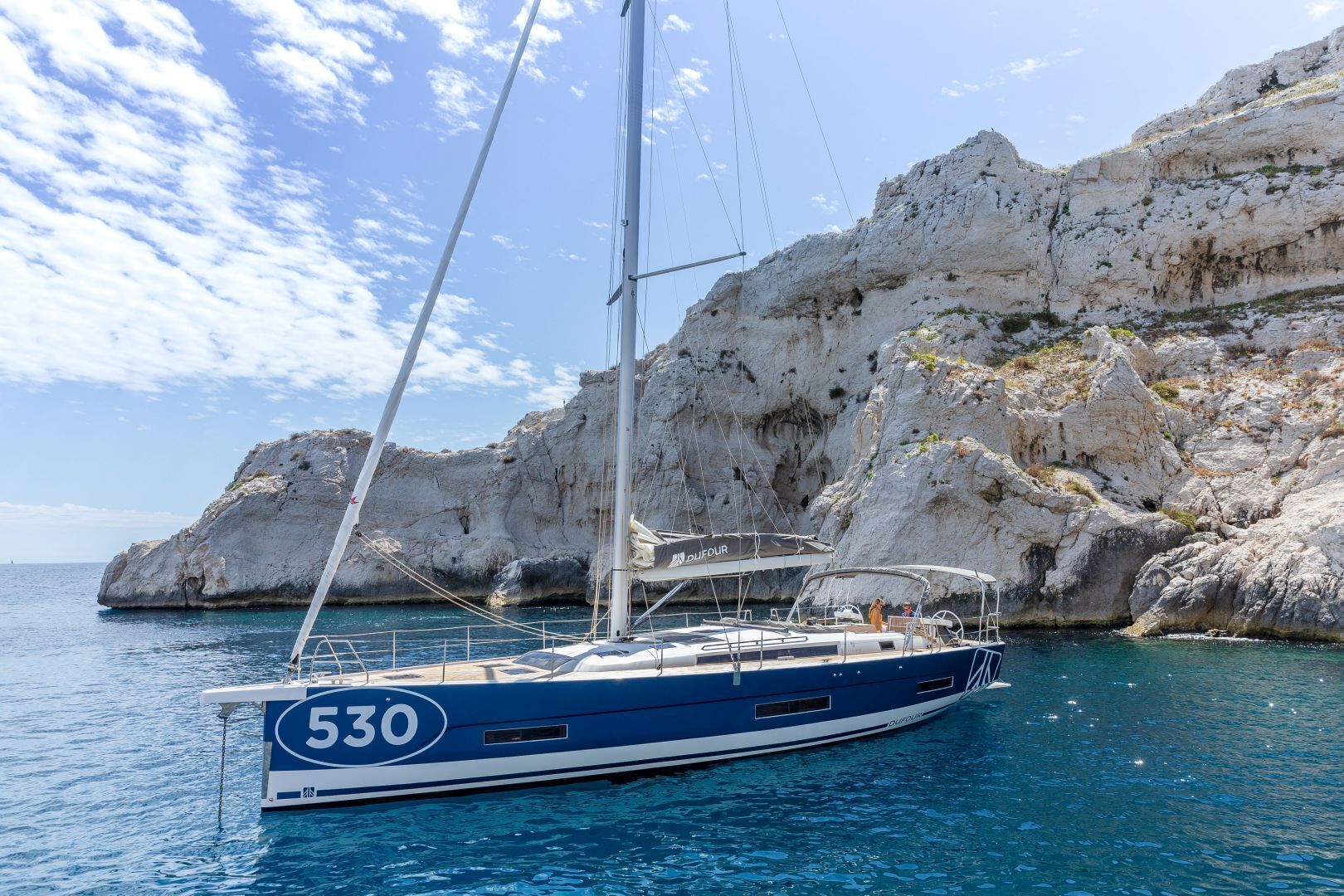A sailboat with the number 530 anchored near rocky cliffs.