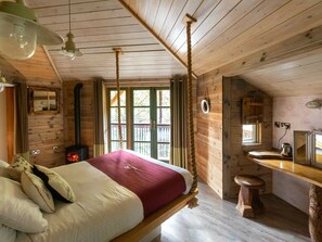 Interior de una cabaña de madera con una cama, una estufa, un lavabo y una ventana.