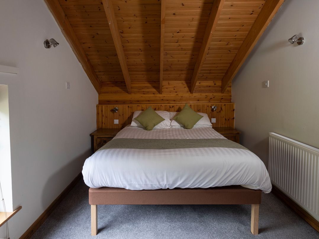 Een slaapkamer met een houten plafond, een bed met witte beddengoed en een radiator aan de muur.