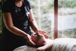 Uma pessoa recebe uma massagem em um quarto com janela que oferece vista para o verde lá fora.