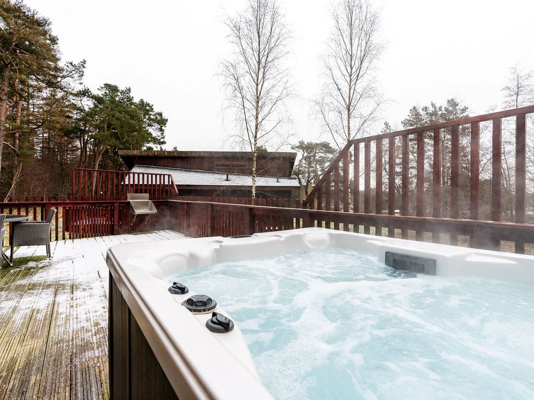 A hot tub with a wooden deck and a metal railing, surrounded by trees.