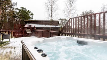 A hot tub with a wooden deck and a metal railing, surrounded by trees.