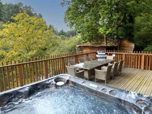 A hot tub with a wooden deck, surrounded by a wooden fence, and a dining area with wicker furniture.