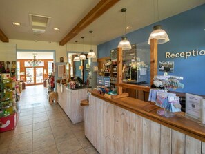 A reception area with a wooden counter, hanging pendant lights, a blue wall with the word 'Reception' visible, and various items on display.