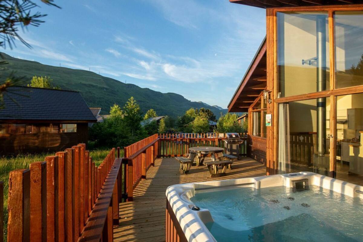 Una terraza de madera con un jacuzzi, asientos exteriores y vistas a montañas.