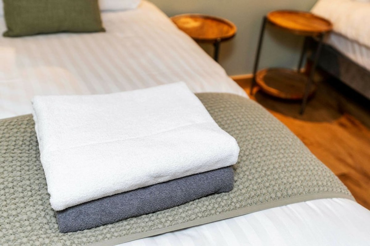 A neatly made bed with a folded white and gray towel on a textured mat.