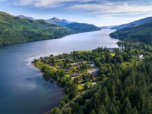 A lakeside resort with multiple cabins and a central building, surrounded by dense forest and hills.