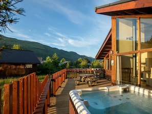 A wooden deck with a hot tub, outdoor seating, and a view of mountains.