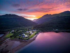 A lakeside resort with cabins and a central building, surrounded by forested hills.