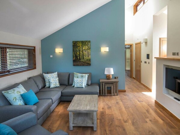 A living room with a sectional sofa, a coffee table, and a painting on the wall. - Ardgartan Argyll - Forest Holidays (Arrochar)