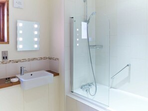 A bathroom with a glass-enclosed shower, a sink with a mirror, and a tiled wall.