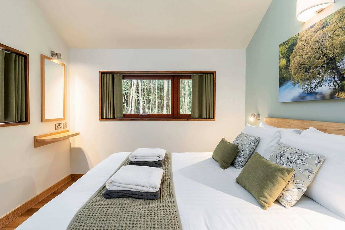 Une chambre à coucher avec un lit, une fenêtre avec des rideaux, un luminaire fixé au mur et un tableau.