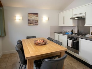 A modern kitchen with white cabinets, a wooden dining table, and two wall-mounted light fixtures. - Glentress Forest - Forest Holidays (Peebles)