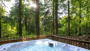 A hot tub surrounded by a wooden deck and dense forest.