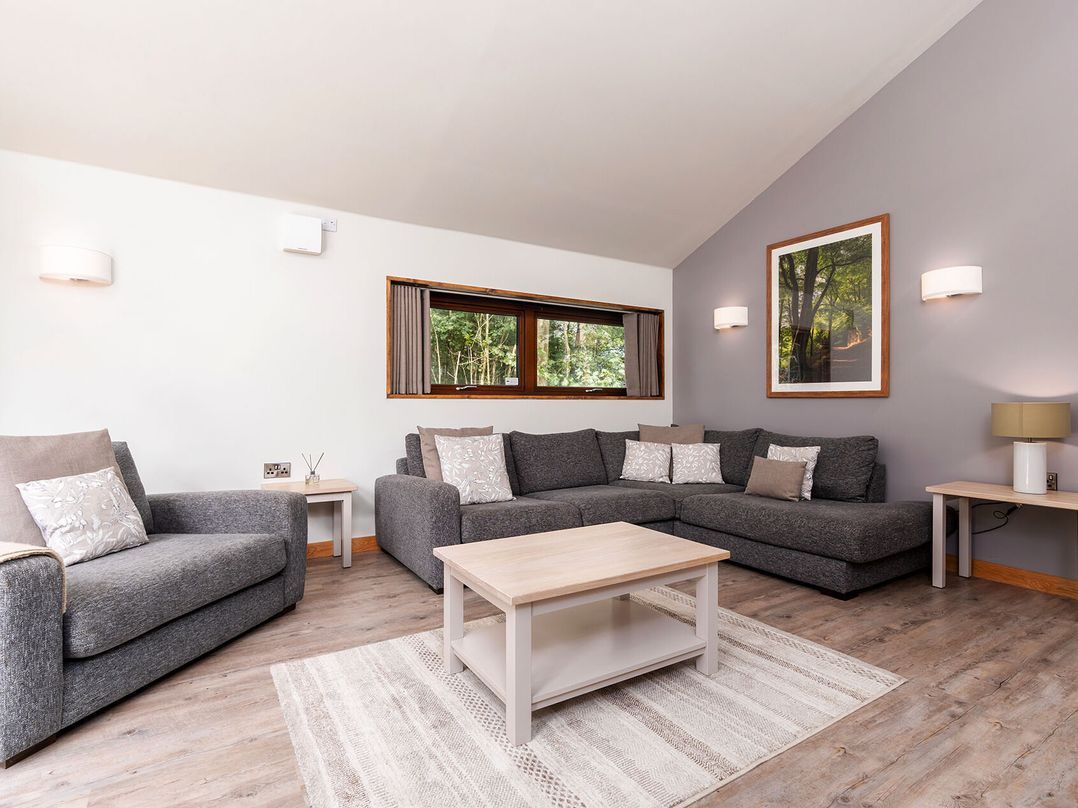 A modern living room with a grey sofa set, a wooden coffee table, and a large window with curtains.