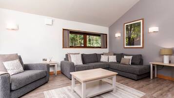A modern living room with a grey sofa set, a wooden coffee table, and a large window with curtains.