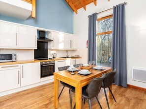A modern kitchen with white cabinets, a wooden dining table, and a view of trees through a window. - Strathyre, Ben Ledi - Forest Holidays (Callander)