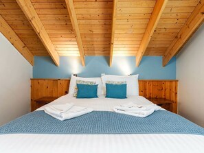 Ein Schlafzimmer mit Holzboden, einem Bett mit blauer Bettwäsche und zwei Nachttischen.