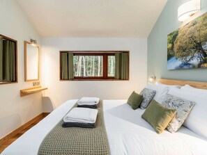Quarto de hotel com cama, janela com cortinas, luminária na parede e um quadro.